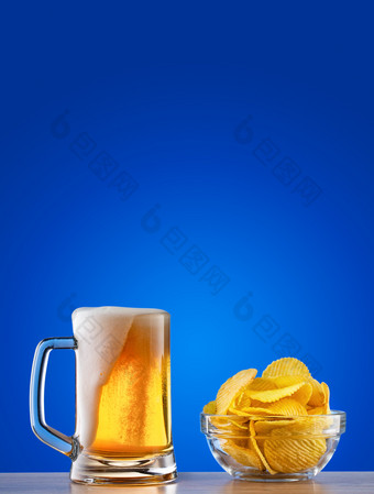 杯子光啤酒与泡沫和芯片蓝色的背景杯子光啤酒与泡沫和芯片蓝色的背景