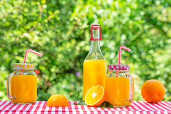 瓶和罐橙色汁与橙子网纹桌布自然绿色背景环保玻璃器皿瓶和罐橙色汁与橙子网纹桌布