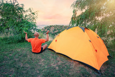 男人。实践瑜伽附近橙色帐篷山男人。橙色t恤坐在体式附近旅游帐篷黎明概念旅行自由和隐私男人。实践瑜伽附近橙色帐篷山