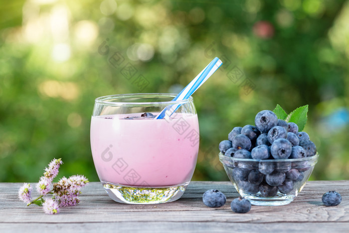 蓝莓奶昔酸奶玻璃杯与稻草和浆果木表格的概念排毒和健康的自然营养蓝莓奶昔酸奶玻璃杯与稻草和浆果