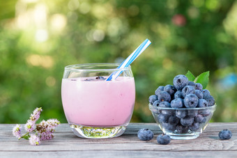 蓝莓奶昔酸奶玻璃杯与稻草和浆果木表格的概念排毒和健康的自然营养蓝莓奶昔酸奶玻璃杯与稻草和浆果