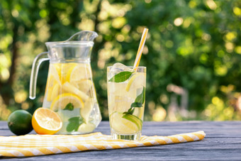 柠檬水壶和玻璃和柠檬与石灰木表格自然绿色背景夏天让人耳目一新喝柠檬水壶和玻璃和柠檬与石灰木表格