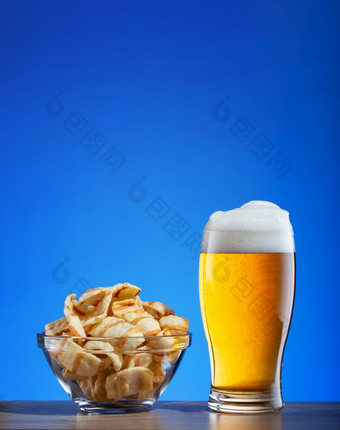 玻璃光啤酒和芯片与培根蓝色的背景啤酒和零食木表格玻璃光啤酒和芯片与培根