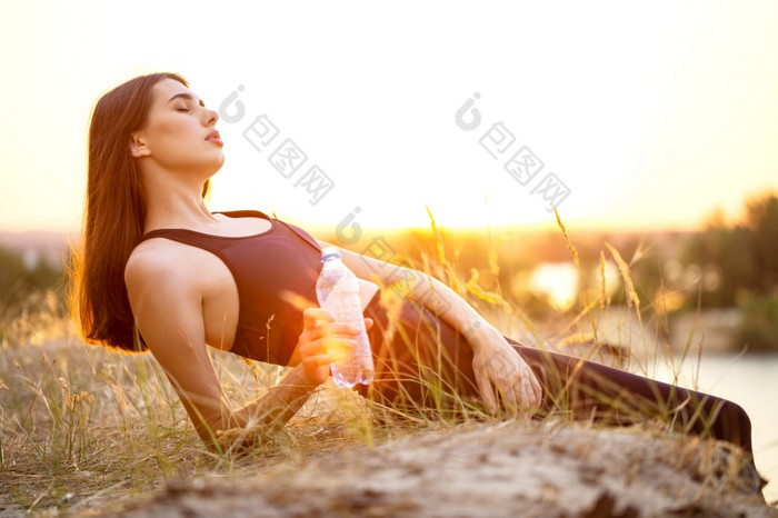 累了女孩运动员谎言的草与关闭眼睛和瓶水她的手的女孩眼睛是关闭日落回来太阳累了女孩运动员谎言草与关闭眼睛和瓶水她的手