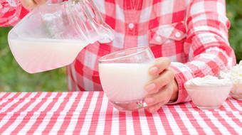 女人倒牛奶从壶成玻璃表格与红色的桌布的表格是乳制品产品自然绿色背景女人倒牛奶从壶成玻璃