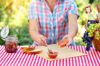 女人格子衬衫涂片小时面包与勺子红色的桌布野餐篮子葡萄阳光明媚的一天野餐概念女人格子衬衫涂片小时面包与勺子