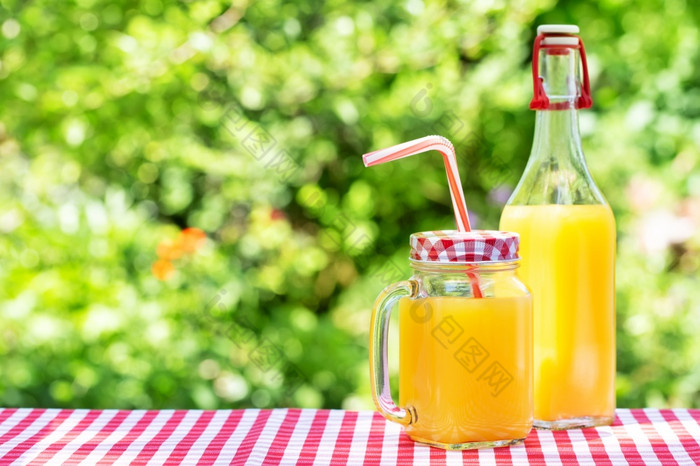 橙色汁梅森罐子和瓶木表格自然绿色背景橙色汁梅森罐子和瓶木表格