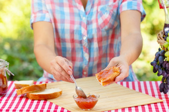 女人格子衬衫涂片小时面包与勺子红色的桌布野餐篮子葡萄阳光明媚的一天野餐概念女人格子衬衫涂片小时面包与勺子