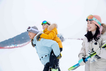 滑雪场上背着儿子的父亲和抱着滑雪板的母亲
