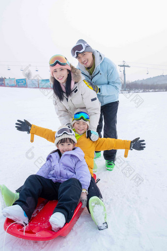 滑雪场上父母推着坐在雪上滑板的孩子们