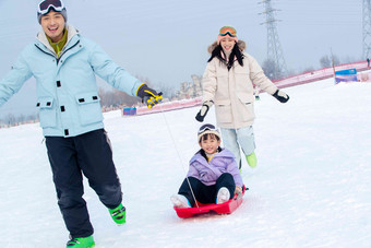 滑雪场上父母和坐在雪上滑板的女儿玩耍