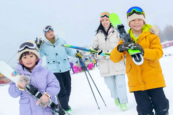 雪场上<strong>拿着</strong>雪具去滑雪的一家四口男孩高质量摄影图