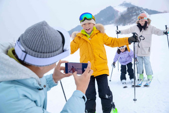 滑雪场上父亲用手机给孩子们和妻子拍照