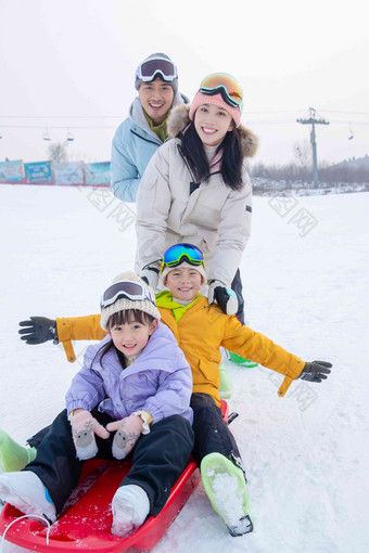 滑雪场上父母推着坐在雪上滑板的孩子们