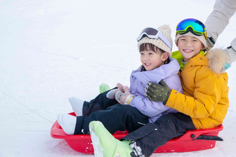 雪场上推着坐在雪上滑板的孩子们