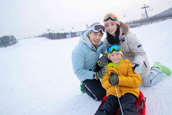 滑雪场上父母和坐在雪上滑板的儿子
