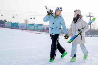 青年伴侣手牵手拿着雪具在滑雪场行走