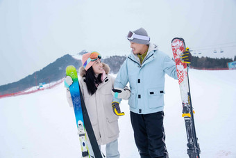 青年伴侣挽着手扶着滑雪板站在雪地上