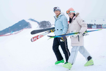 青年伴侣手牵手拿着雪具在滑雪场行走