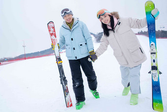 青年伴侣手牵手扶着滑雪板站在雪地上成年人氛围摄影