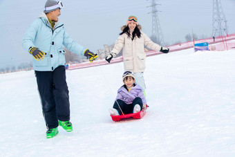 <strong>滑雪</strong>场上父母和坐在雪上滑板的女儿玩耍