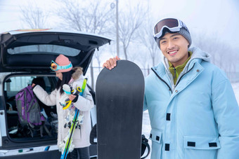 汽车后的青年伴侣拿着滑雪板