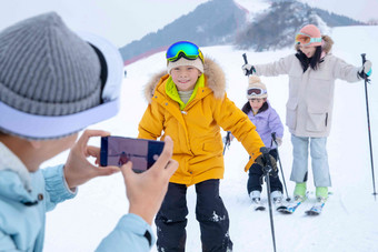 滑雪场上父亲用手机给孩子们和妻子拍照