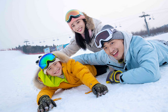 快乐的一家三口趴在雪地上玩雪温馨高清素材