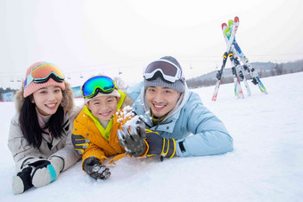 快乐的一家三口趴在雪地上玩雪独生子女家庭高端镜头