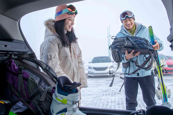 停车场内青年伴侣拿着背包雪具交谈雪写实摄影