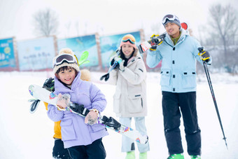 雪场上拿着雪具去滑雪的一家四口