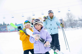 雪场上拿着雪具去滑雪的一家四口