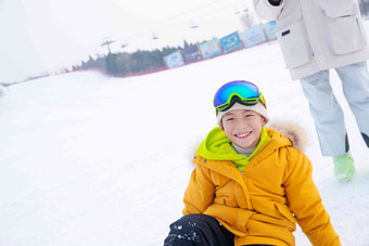 雪场上坐在雪地上的快乐男孩