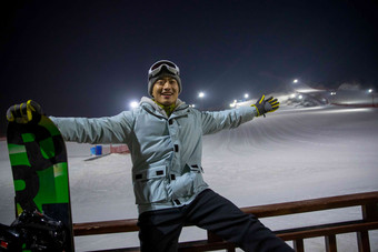 夜晚青年男人坐在滑雪场内的护栏上