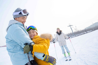 滑雪场上抱在一起的父子和滑雪的母亲冬天氛围图片