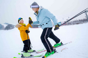 滑雪场上滑着雪击掌的快乐父子雪地高质量摄影图