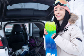 青年女人拿着<strong>滑雪</strong>板站在汽车后备箱旁