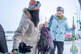 停车场内青年伴侣拿着雪具交谈