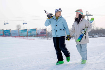 青年伴侣手牵手拿着<strong>滑雪</strong>板边走边聊