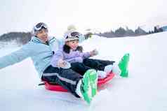 滑雪场上快乐父女坐着雪上滑板滑雪