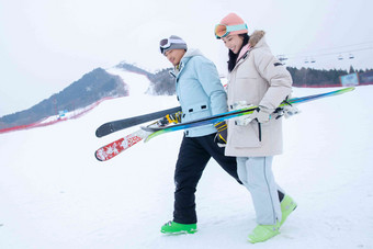 青年伴侣手牵手拿着雪具在滑雪场行走
