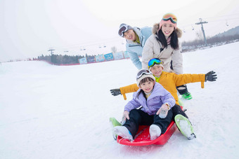 滑雪场上父母推着坐在雪上滑板的孩子们母亲高清摄影图