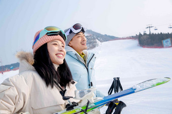 雪场上拿着滑雪板滑雪杖的快乐情侣