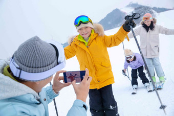 滑雪场上父亲用手机给孩子们和妻子拍照