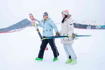 青年伴侣手牵手拿着滑雪板边走边聊