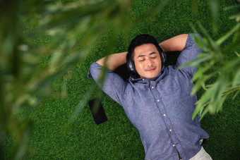 躺在草地上听音乐的青年男人闭着眼睛高质量照片