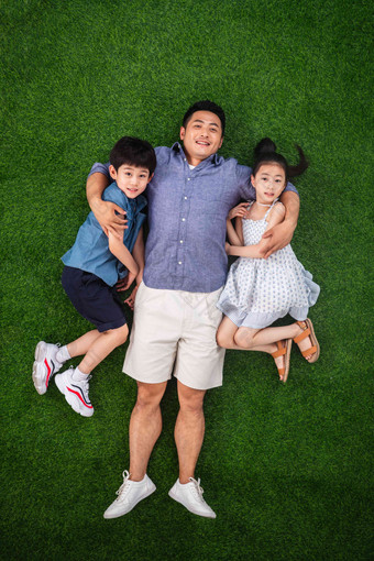 父亲搂着儿子和女儿躺在草地上快乐氛围图片