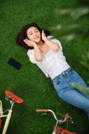 躺在草地上听音乐的年轻女人享乐高端场景