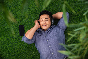 快乐的青年男人躺在草地上听音乐草地高端拍摄