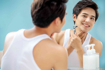 青年男人对着镜子刮胡子微笑的高质量摄影